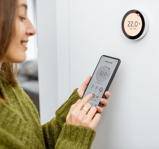woman adjusting smart thermostat using smartphone display showing temperature settings for energy efficiency and temperature control